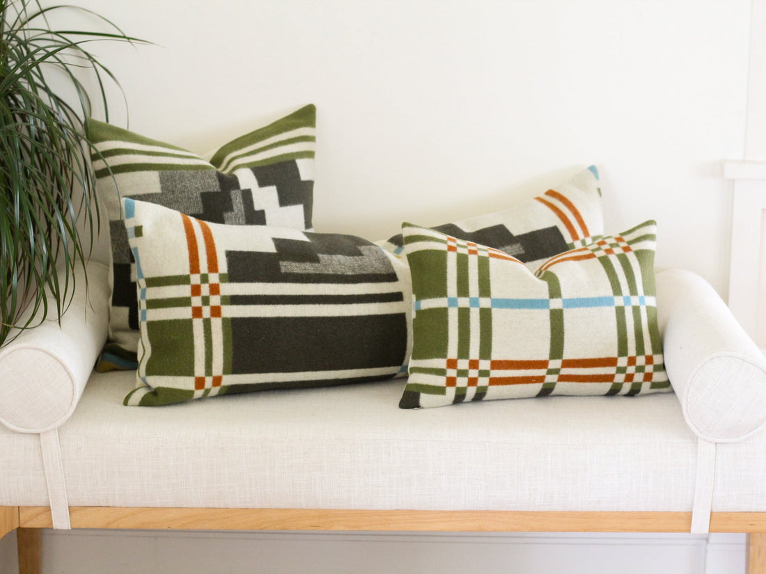 Three pillows sitting on a white bench. The pillows are made with the green and cream Seven Springs Pendleton pattern.