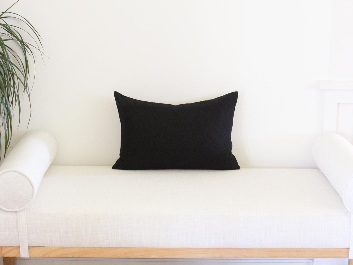 The back of a rectangular decorative throw pillow in solid black wool. The pillow is positioned horizontally, featuring clean, straight edges.