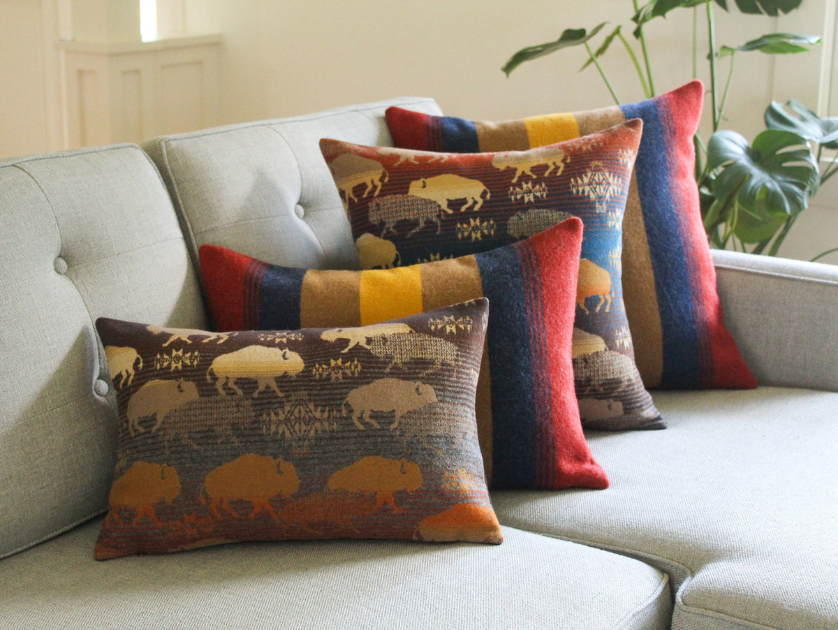 Four decorative wool throw pillows, two with a brown, yellow, red, and blue striped pattern, and two pillows with a design of buffalo silhouettes.