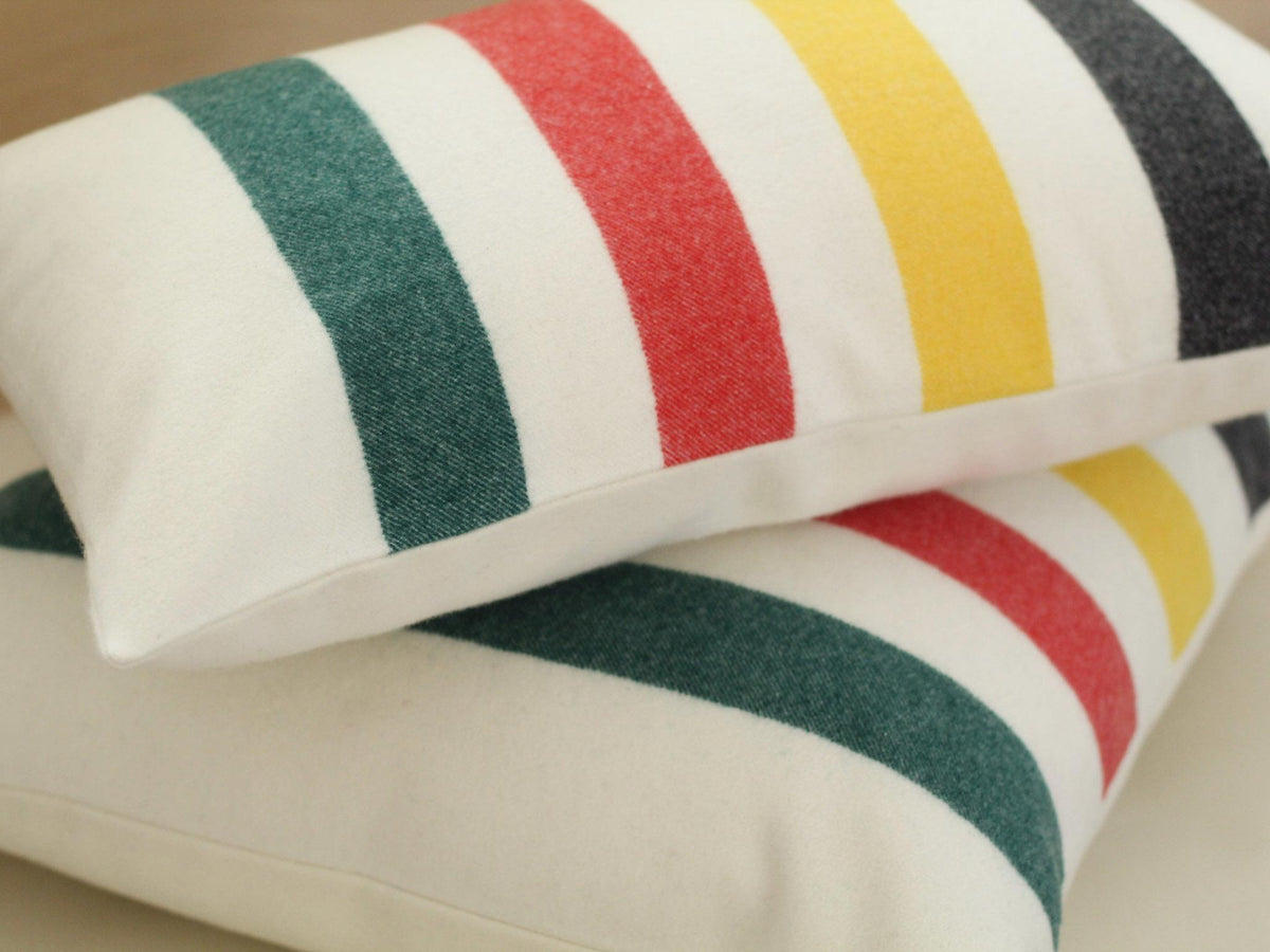 Two rectangular throw pillows with a cream background and bold, colorful stripes. The stripes are in shades of green, red, yellow, and black. The pillows are stacked on top of each other, showcasing the striped pattern.