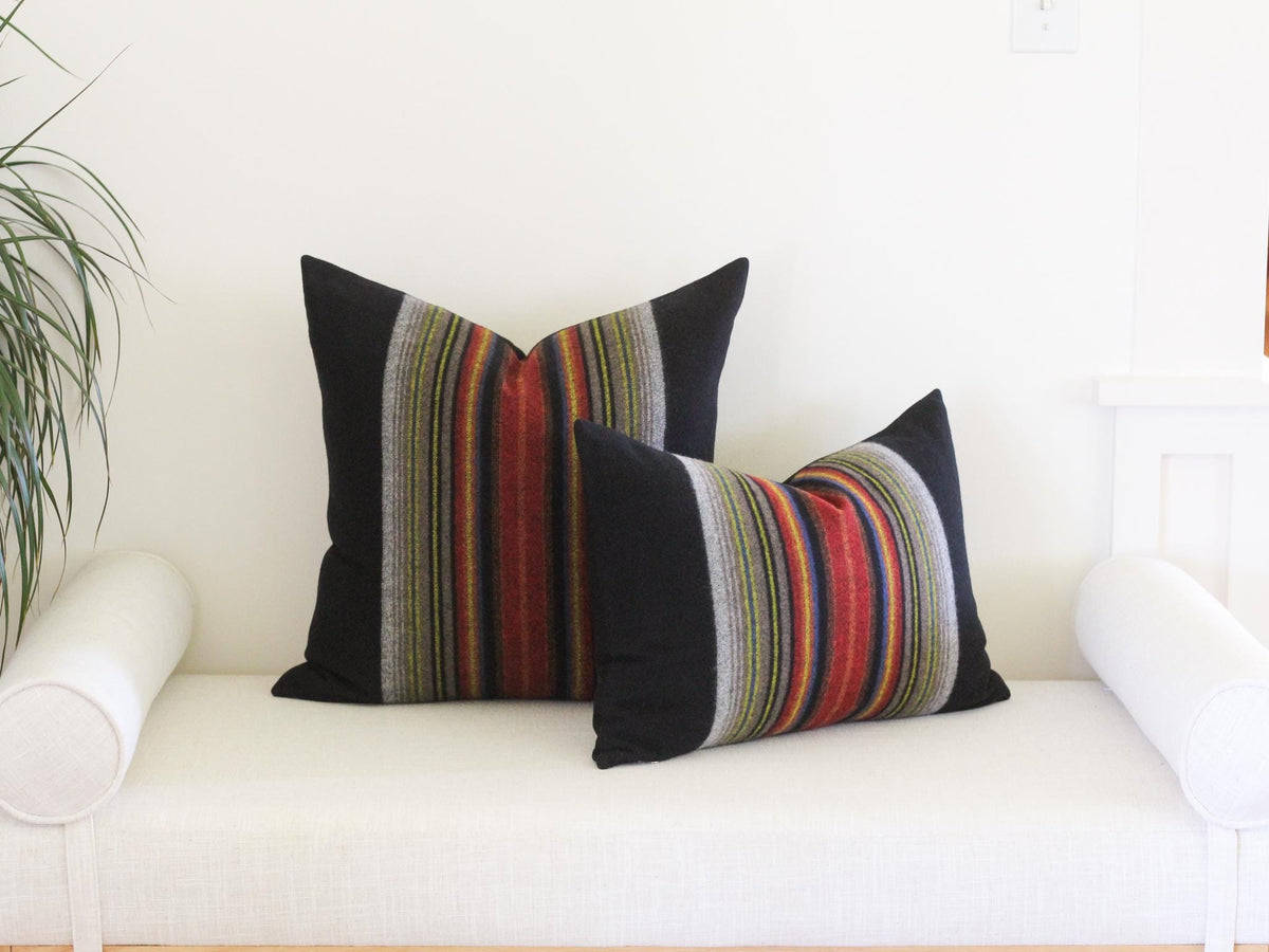 Two square throw pillows featuring a solid black fabric on the outer edges and a central vertical panel with multi-colored stripes in shades of red, orange, yellow, blue, and grey. The pillows have a soft, textured appearance.