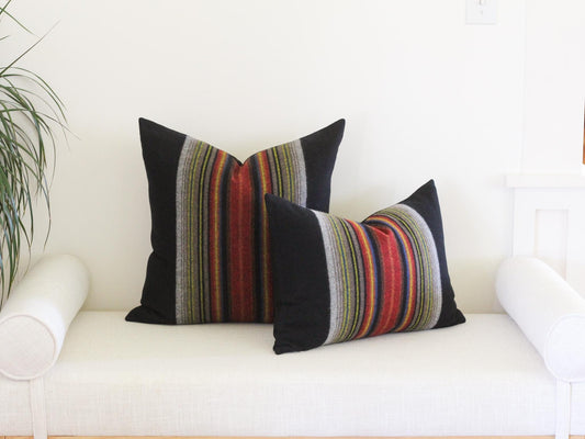 Two square throw pillows featuring a solid black fabric on the outer edges and a central vertical panel with multi-colored stripes in shades of red, orange, yellow, blue, and grey. The pillows have a soft, textured appearance.