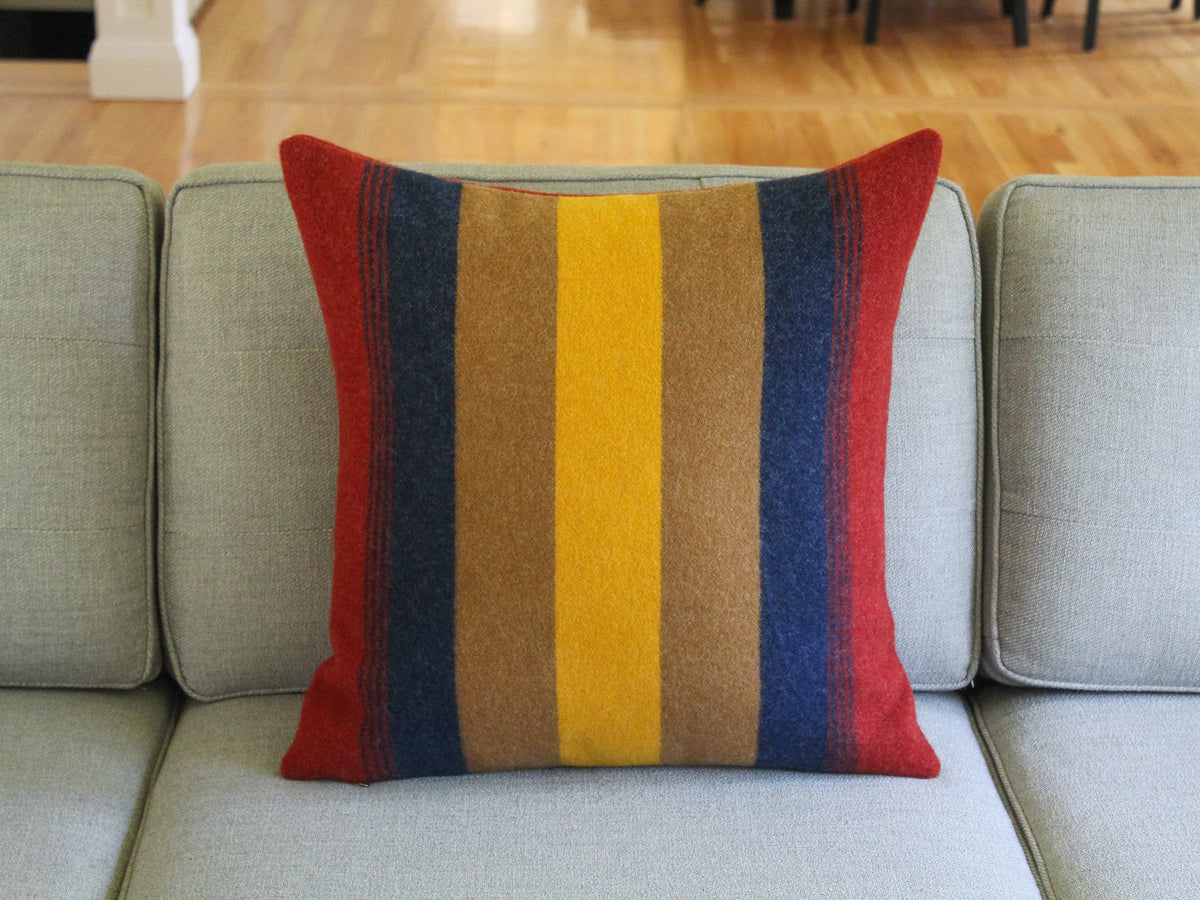 A striped throw pillow with red, yellow, brown, and blue stripes. The pillow is on a gray couch.