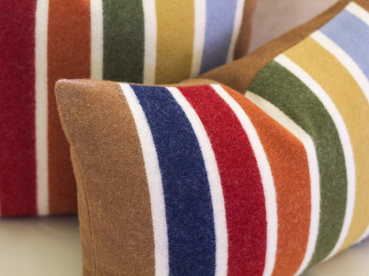 Two striped throw pillows with a camel brown, white, red, blue, green, and yellow color scheme. The pillows are made of wool.