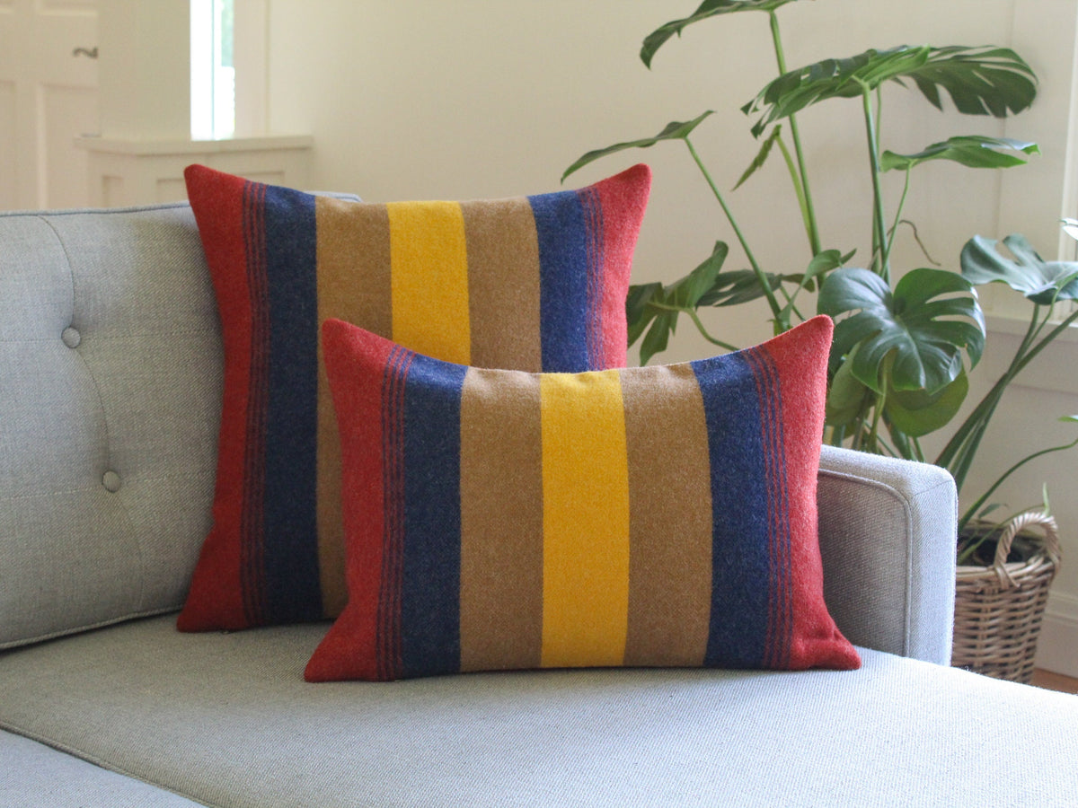 Two decorative throw pillows with a striped pattern in red, yellow, brown, and blue. The pillows are on a gray couch.