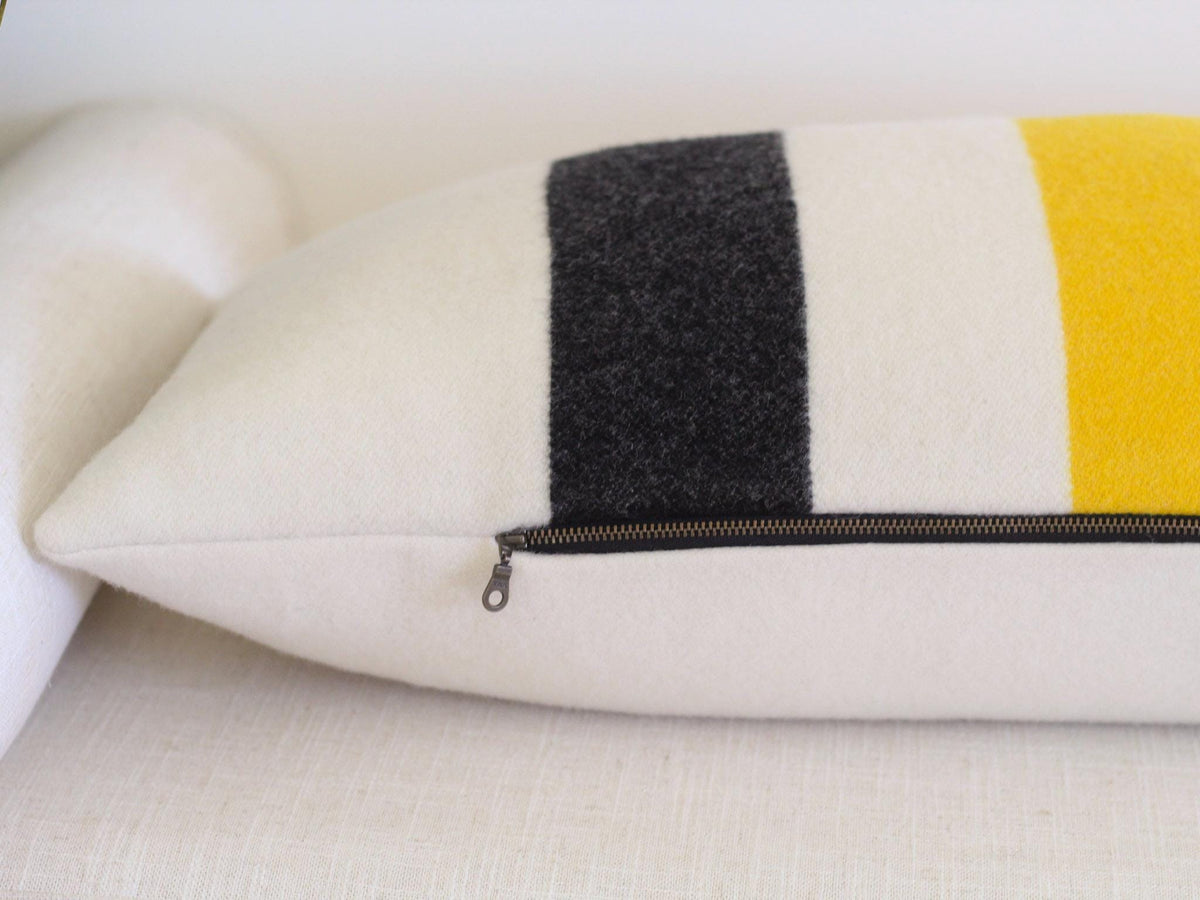 Close up of the bottom seam and zipper on a rectangular lumbar pillow featuring a cream-colored base with vertical stripes in black and yellow.