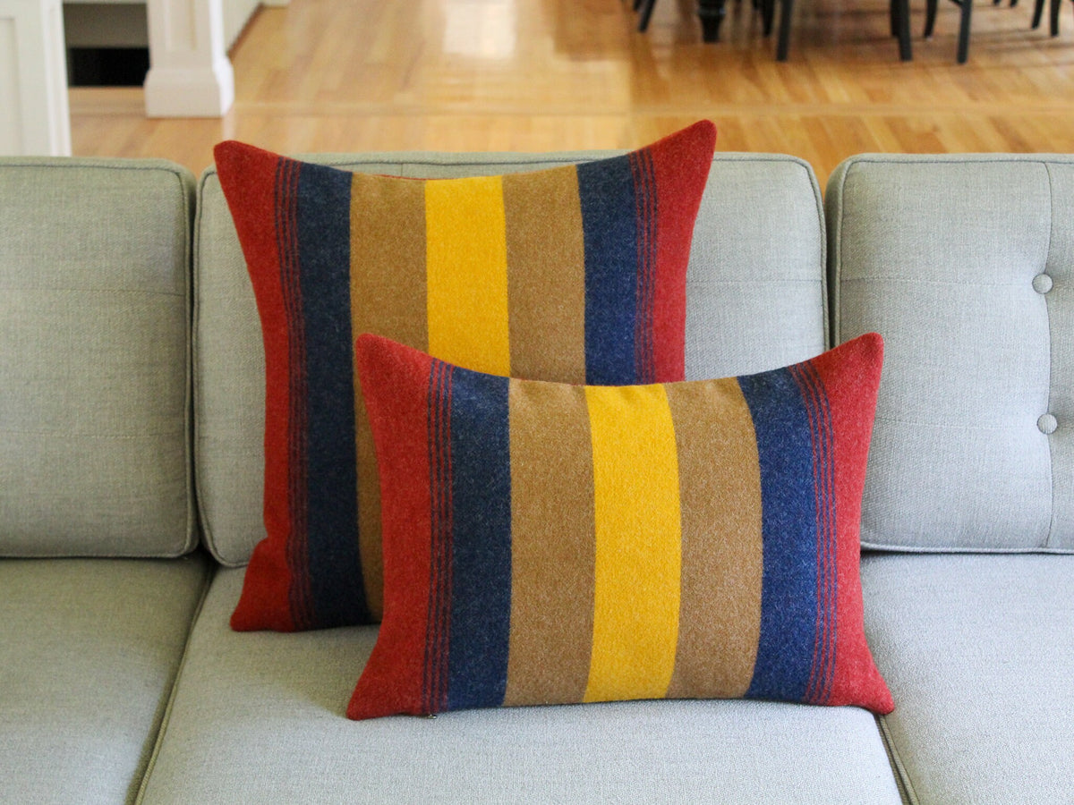 Two striped throw pillows with a red, yellow, brown, and blue color scheme. The pillows are on a gray couch.