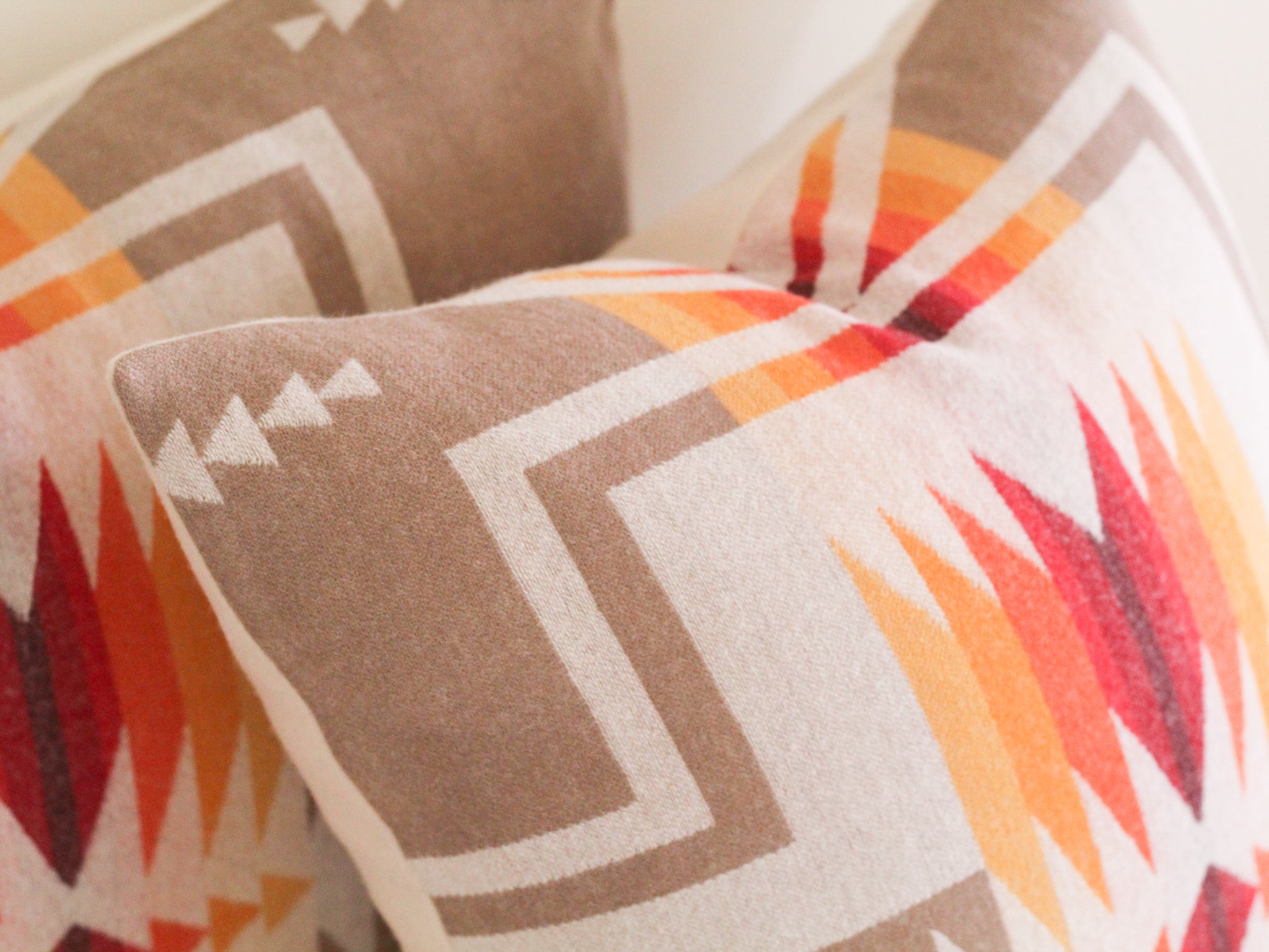 Close up image of two True Having pillow covers in the Harding Tan pattern, which features a native American motif in tan, cream, red, orange, and yellow.