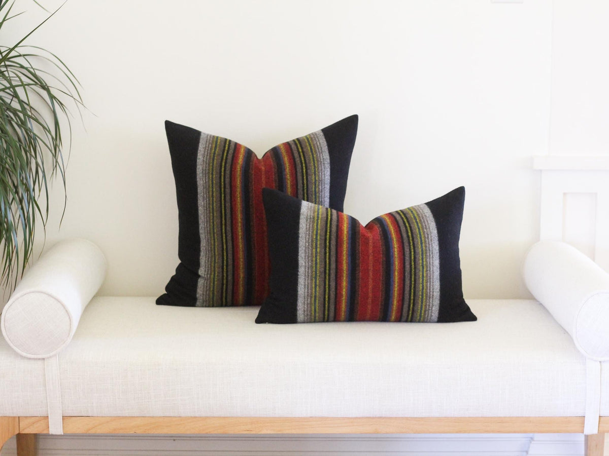 Two rectangular throw pillows featuring a central vertical panel of multi-colored stripes in shades of red, orange, yellow, blue, and grey, flanked by solid black fabric on the outer sides.