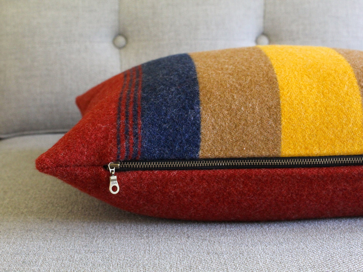 A red, brown, yellow, and blue striped throw pillow with a zipper closure.