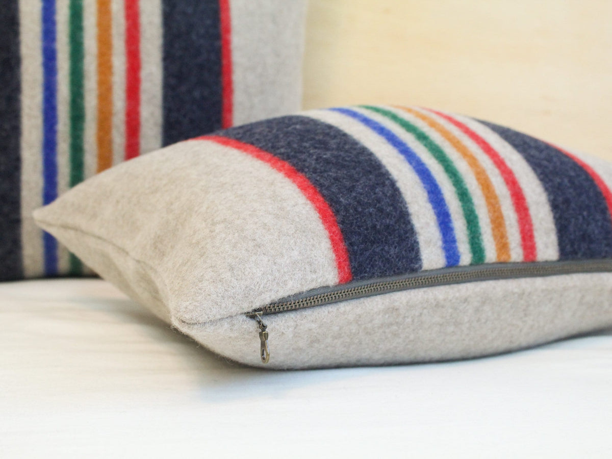 A beige striped throw pillow with a zipper closure. The pillow has a pattern of red, blue, green, and gold stripes.