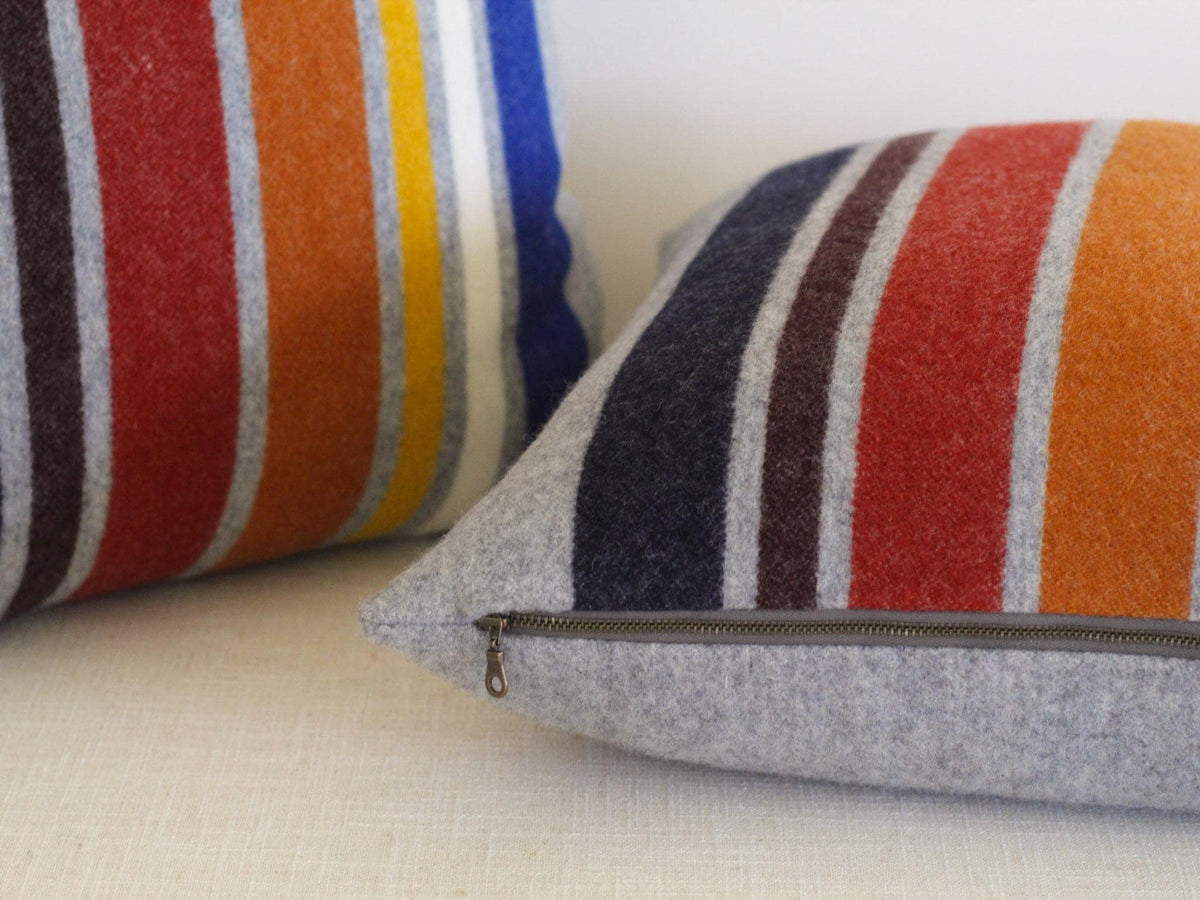 Two decorative throw pillows with a striped pattern. The pillows feature vertical stripes in navy, brown, red, orange, yellow, white, and blue. The pillow covers are gray with a zipper closure.