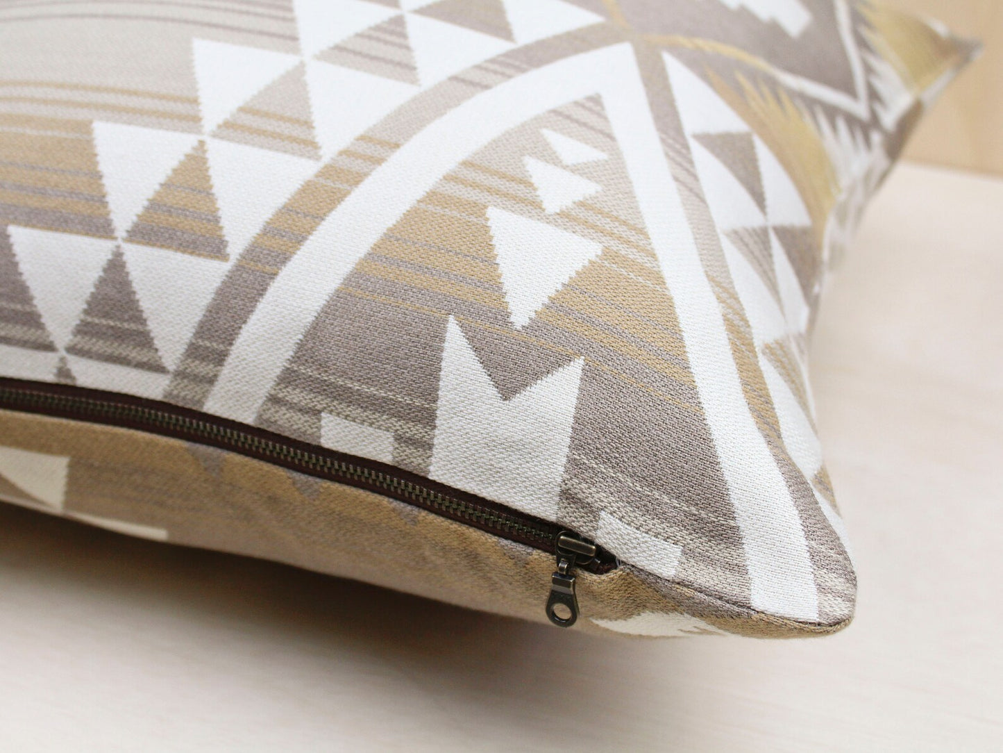 Close up of the exposed metal zipper on an outdoor pillow cover in the cream and tan southwestern Canyonlands pattern.