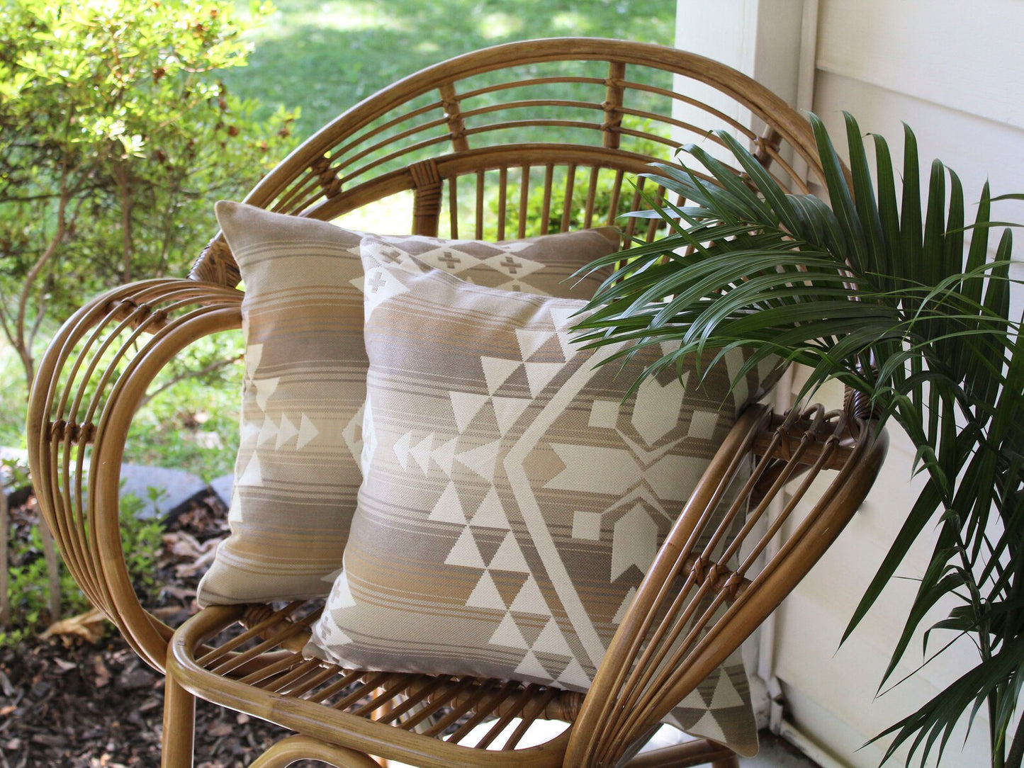 Wicker chair with two outdoor pillow covers and a plant on a porch. The outdoor pillow covers are in the cream and tan southwestern Canyonlands pattern.