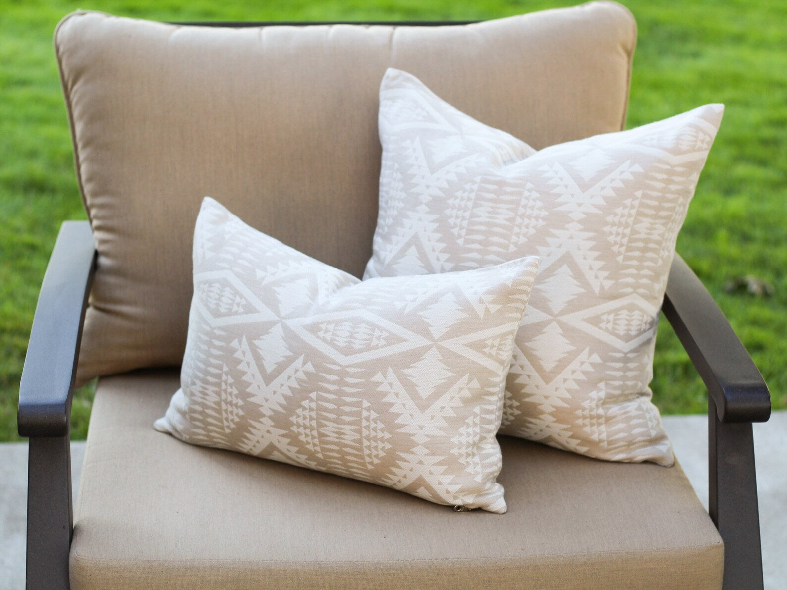 Two outdoor pillows in the two-tone tan River Tonal Sand pattern on a beige outdoor chair with a grassy background