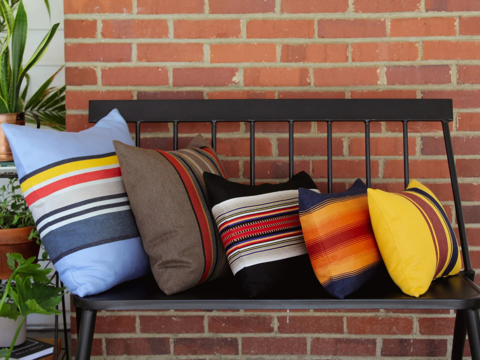 Colorful striped outdoor pillows on a black metal bench against a brick wall.
