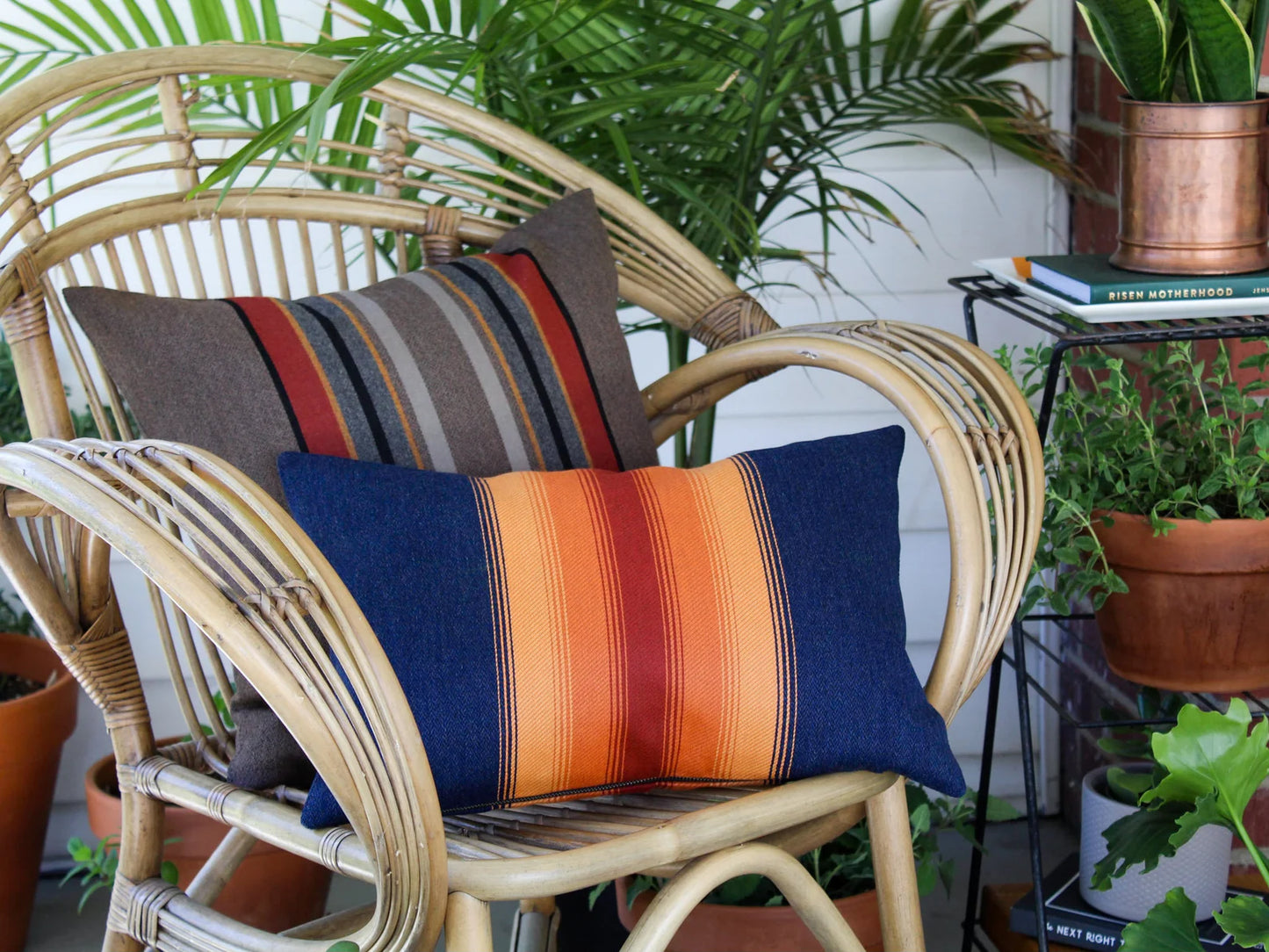 Wicker chair with colorful striped outdoor pillows in an outdoor setting with plants.