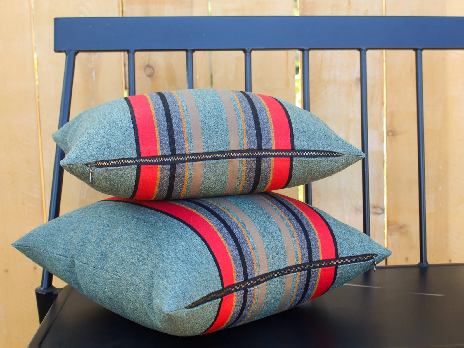 Colorful striped Yakima Park Heather outdoor pillow covers on a black chair against a wooden fence background