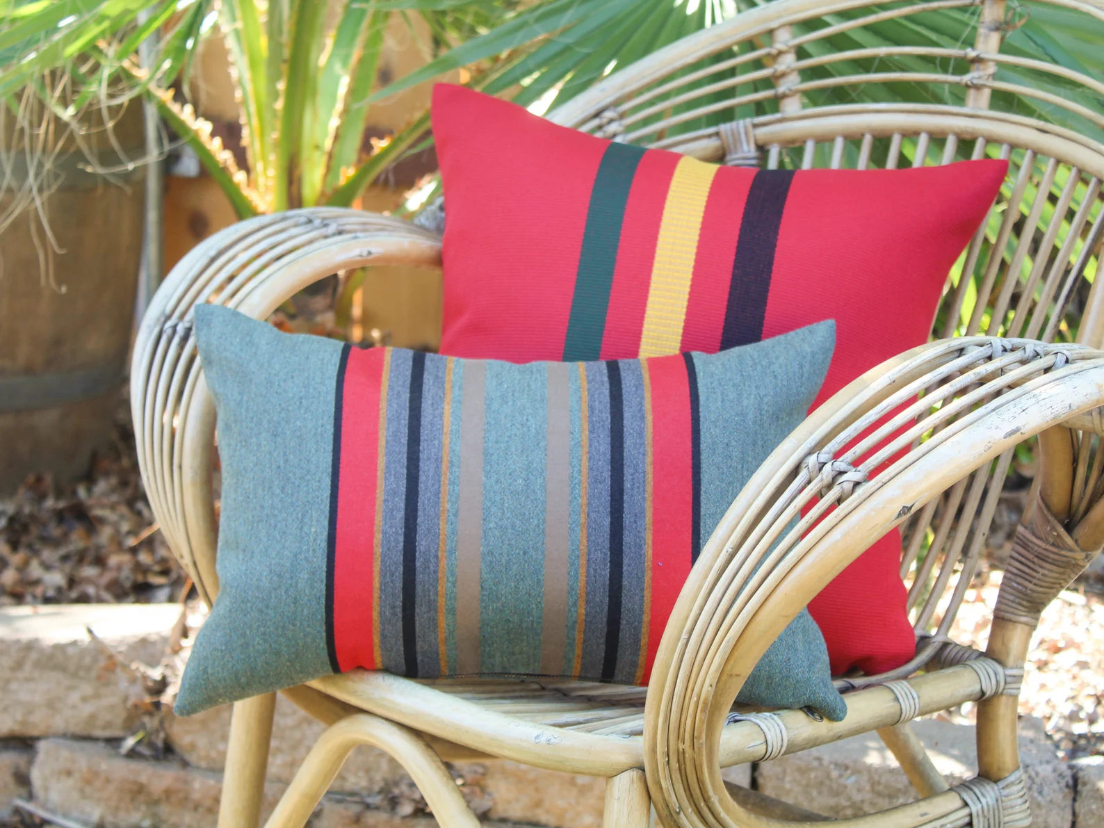 Two striped outdoor pillows on a wicker chair outdoors.
