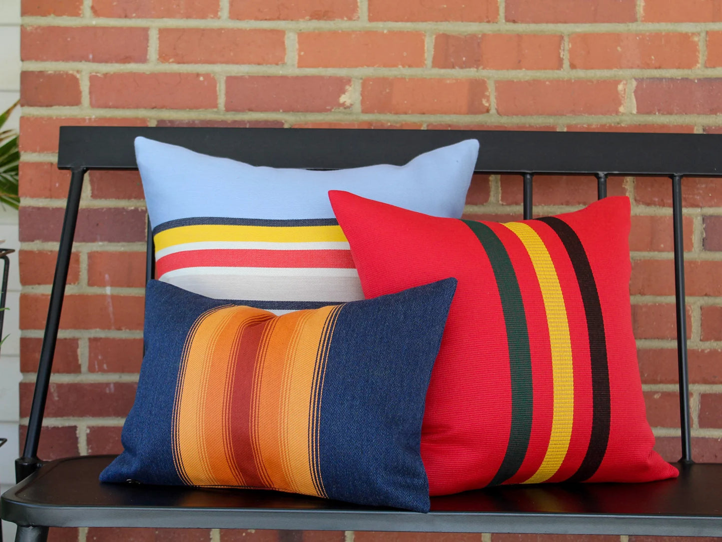 Colorful striped pillows on a bench against a brick wall