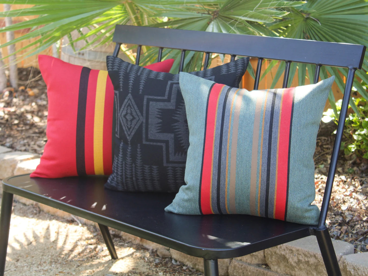 Three patterned outdoor pillows on a black bench with a natural background
