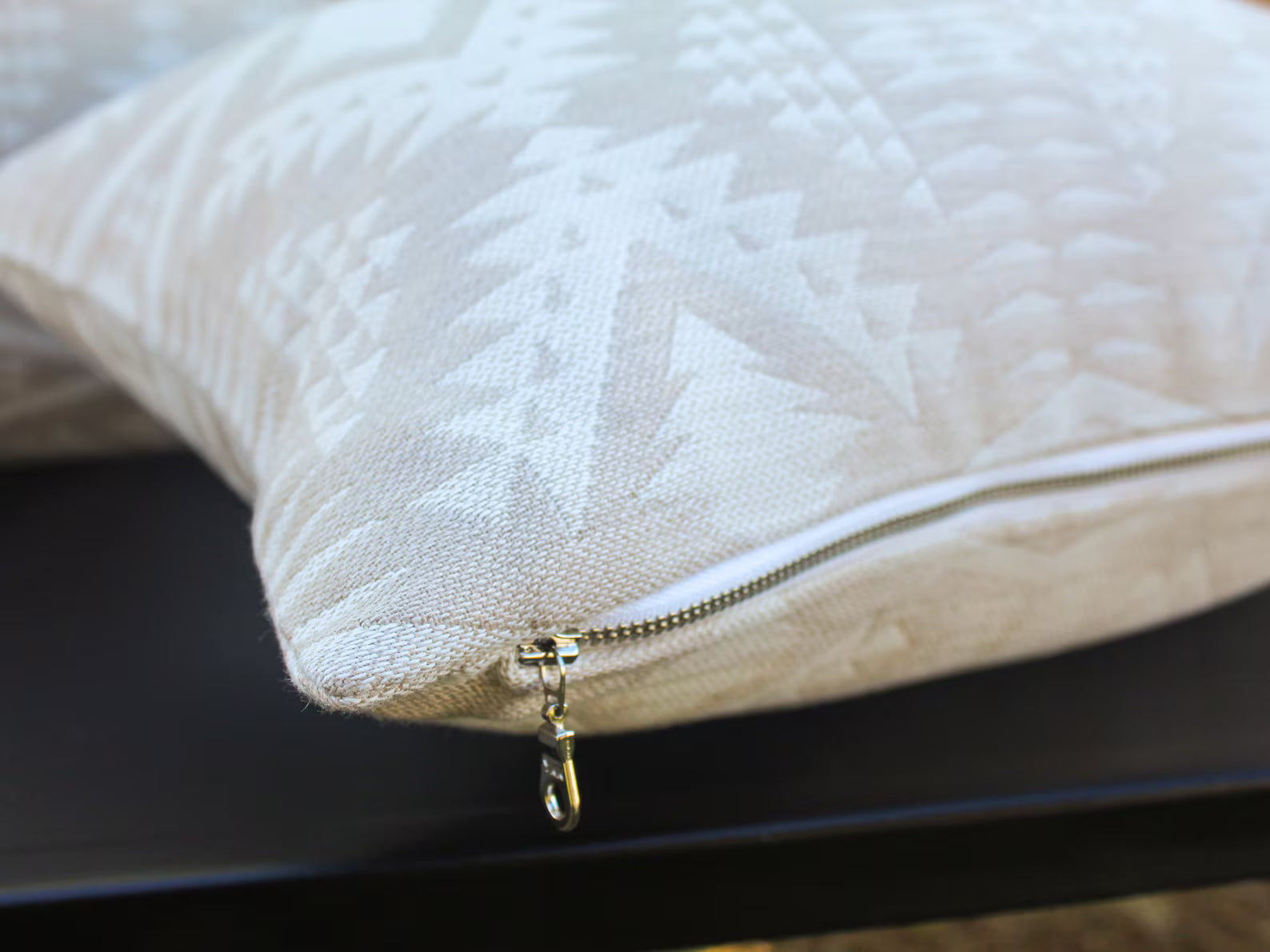 Close-up of an outdoor pillow in the two-tone tan River Tonal Sand pattern with a zipper on a blurred background