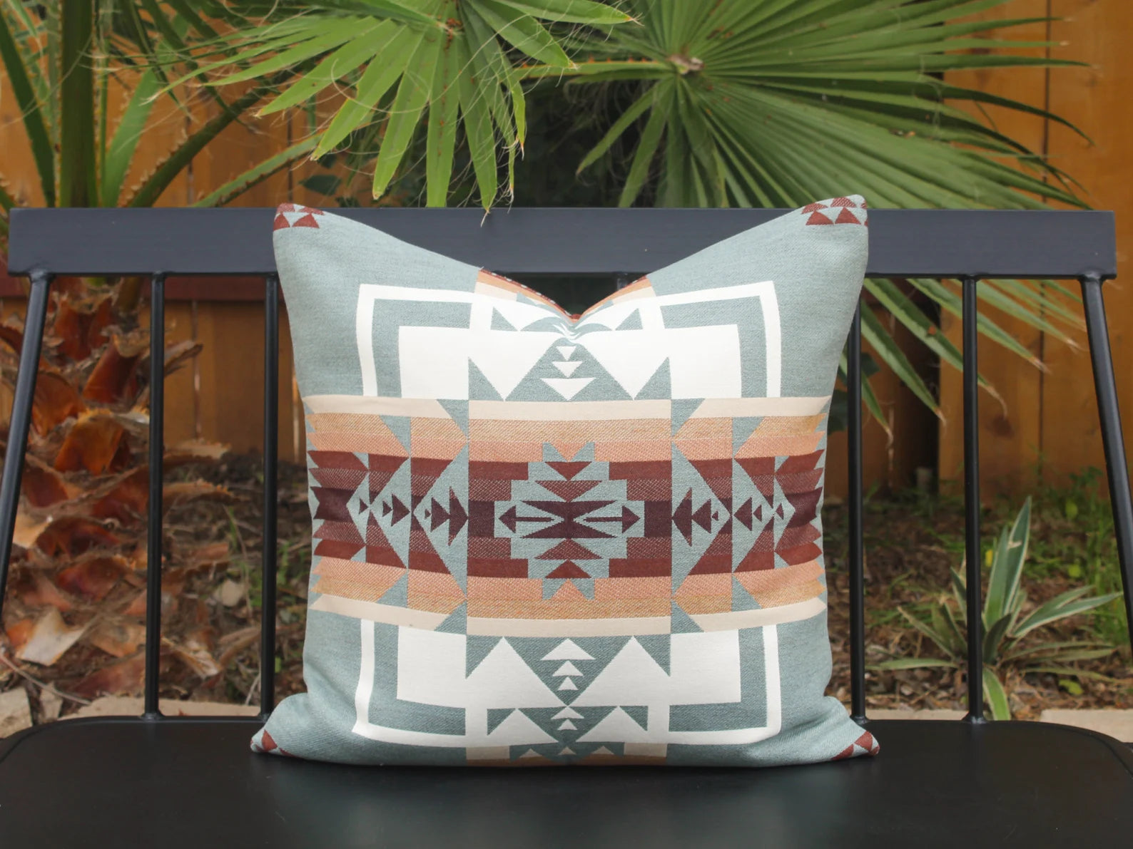 Single outdoor pillow in the blue, brown, and white southwestern Chief Joseph pattern on a bench with a natural background. This photo shows the 22 inch by 22 inch size.