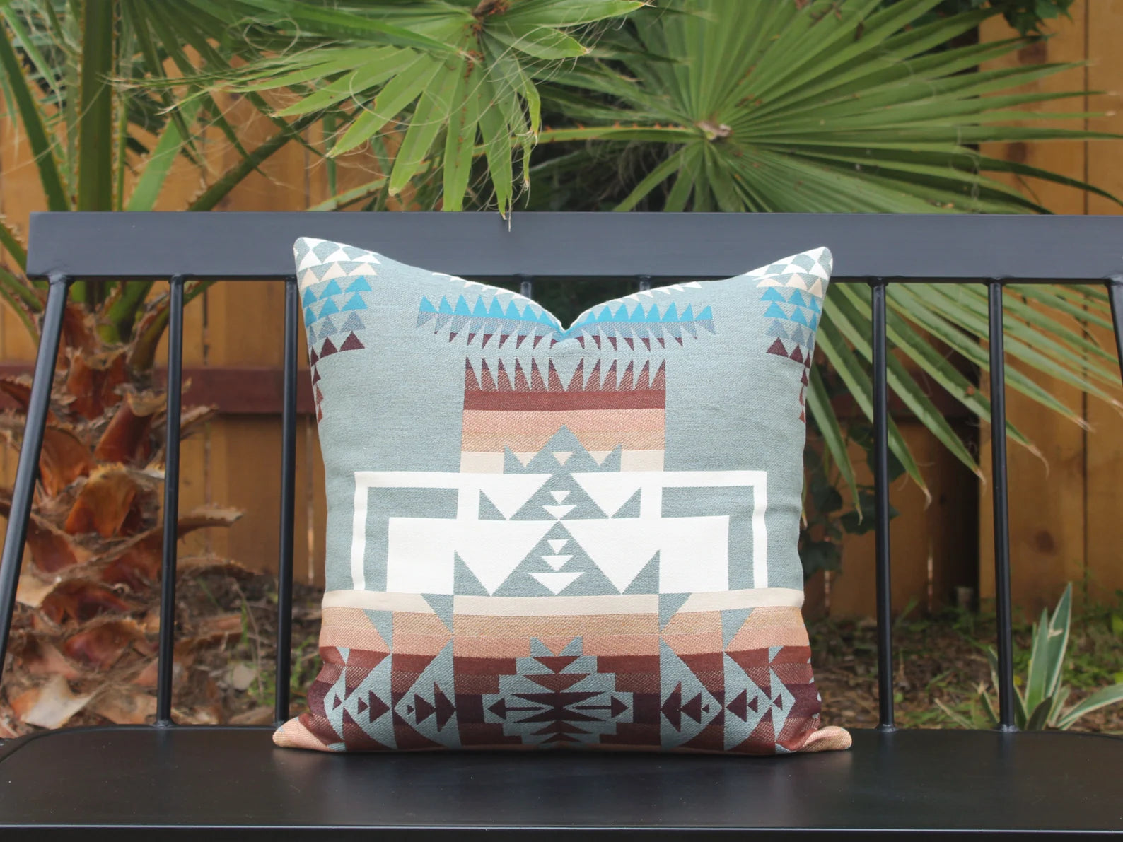 Single outdoor pillow in the blue, brown, and white southwestern Chief Joseph pattern on a bench with a natural background. This photo shows the 20 inch by 20 inch size.