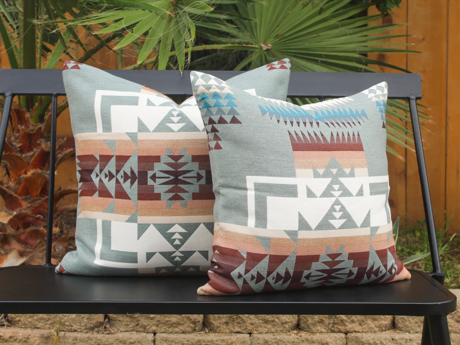 Two outdoor pillows in the blue, brown, and white southwestern Chief Joseph pattern on a bench with a natural background