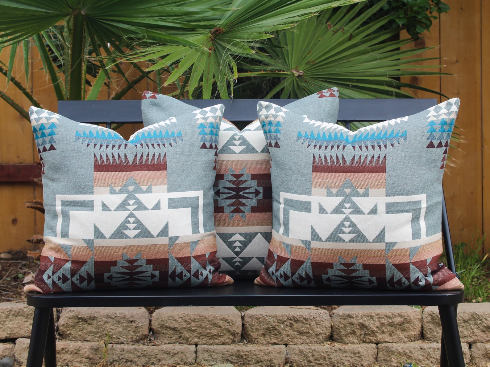 Three outdoor pillows in the blue, brown, and white southwestern Chief Joseph pattern on a bench with a natural background