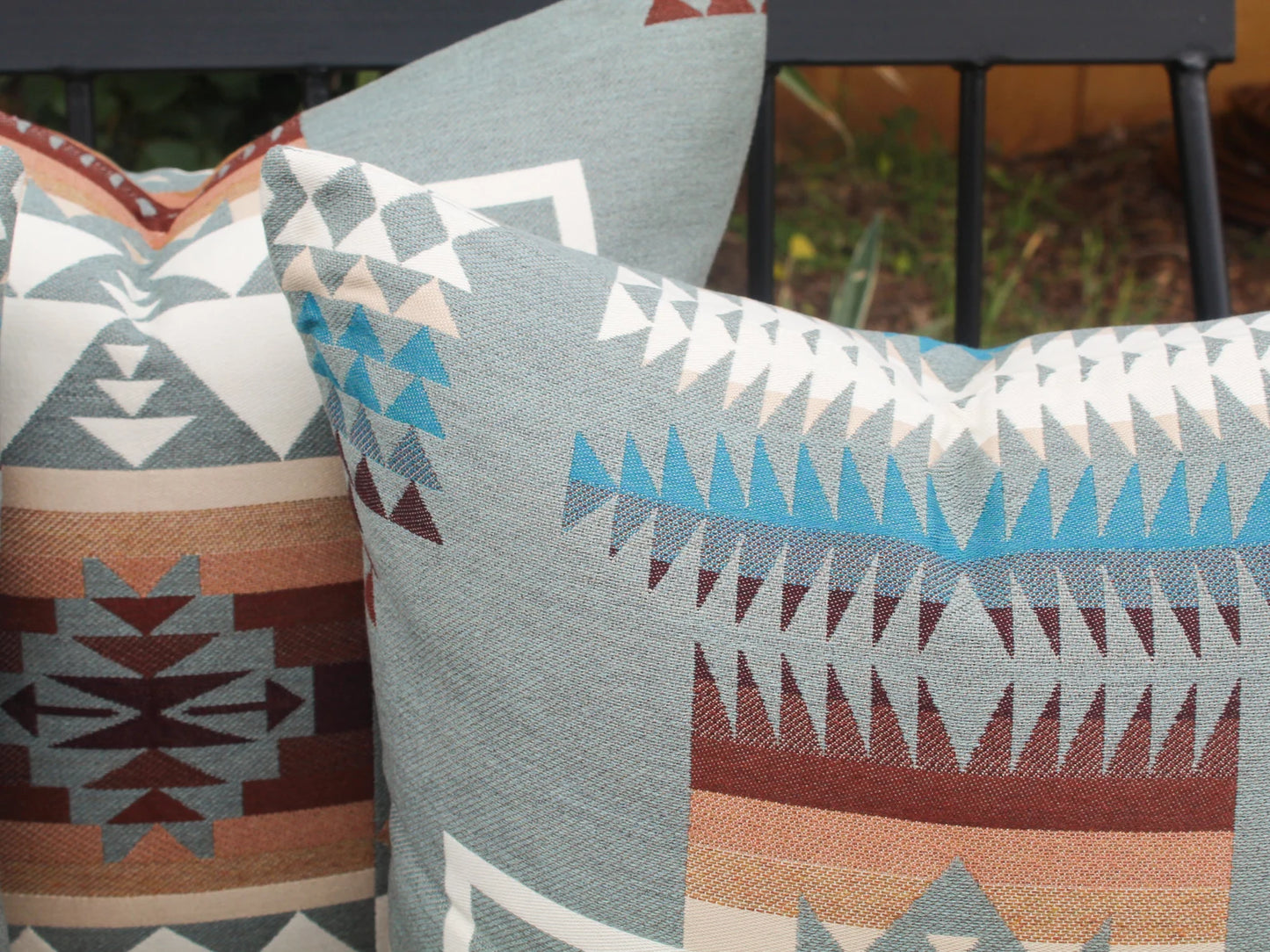 Close up of outdoor pillows in the blue, brown, and white southwestern Chief Joseph pattern on a bench with a natural background
