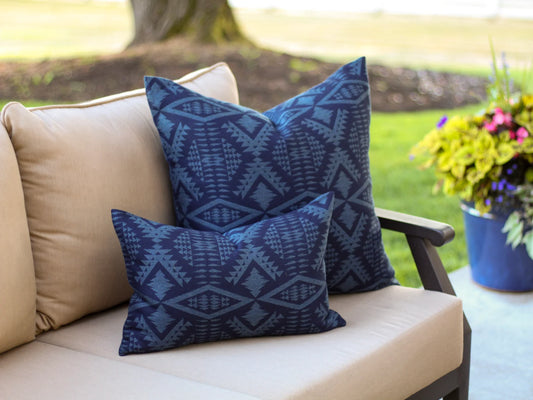 Outdoor pillows in the two-tone blue River Tonal Midnight pattern on a beige outdoor sofa with a blurred garden background