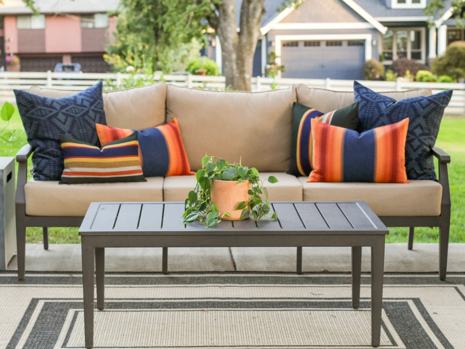 Outdoor patio set with beige sofa, colorful outdoor pillows, and a coffee table on a deck.