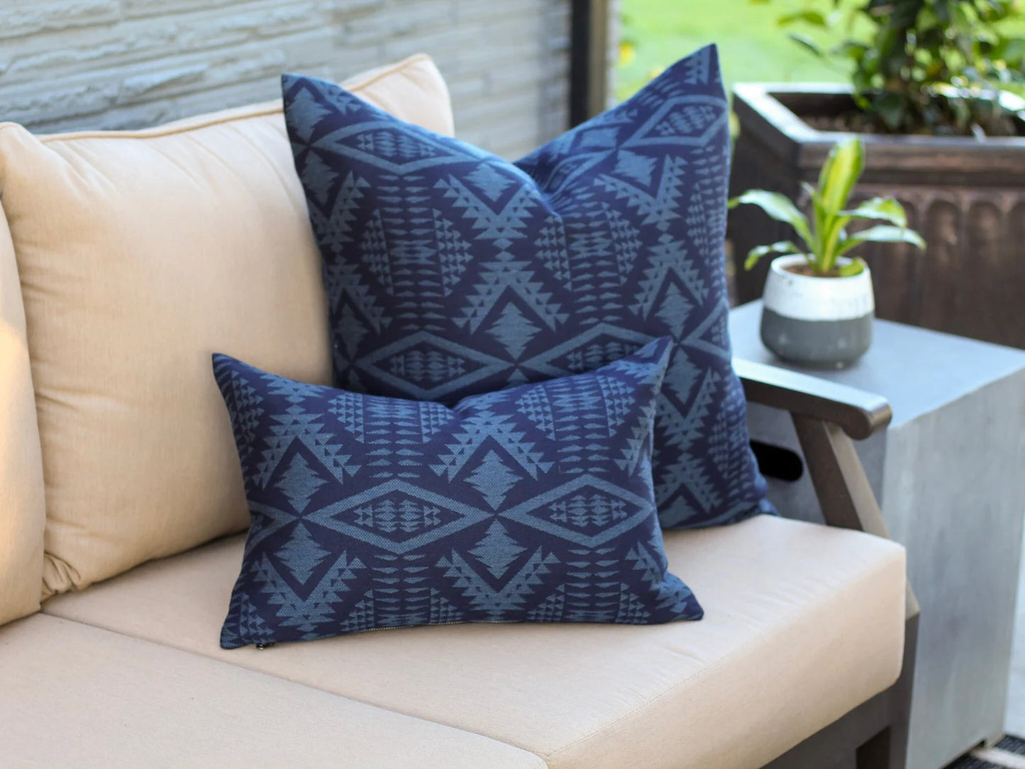 Outdoor pillow in the two-tone blue River Tonal Midnight pattern on a beige outdoor sofa with a blurred background