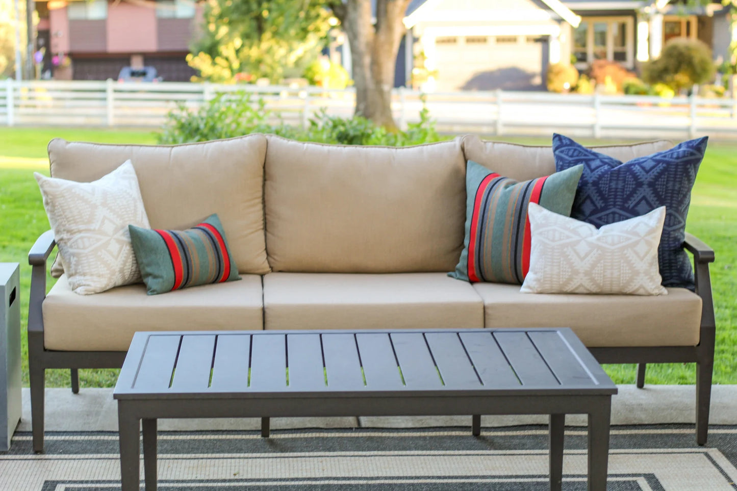 Beige outdoor sofa with colorful outdoor pillows and a matching table on a patio