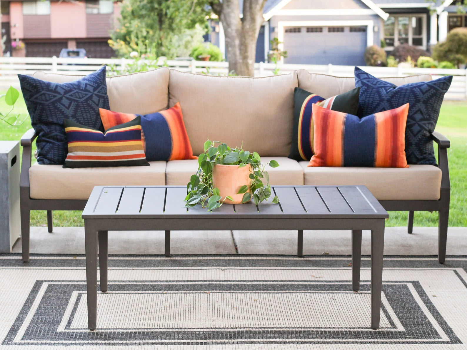 Outdoor patio set with beige sofa, colorful pillows, and a coffee table on a patio.