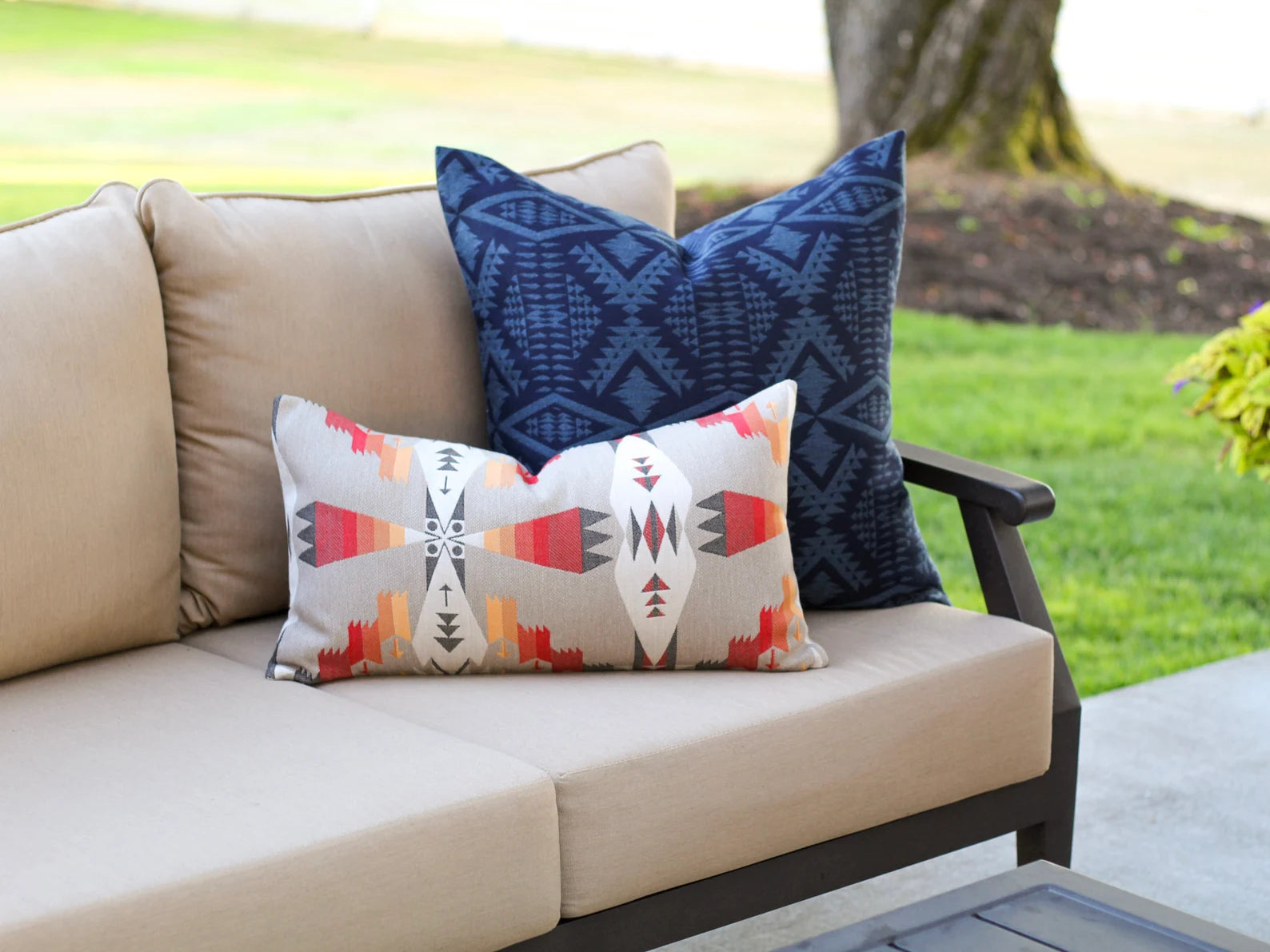 Beige outdoor sofa with patterned outdoor pillow covers against a blurred garden background