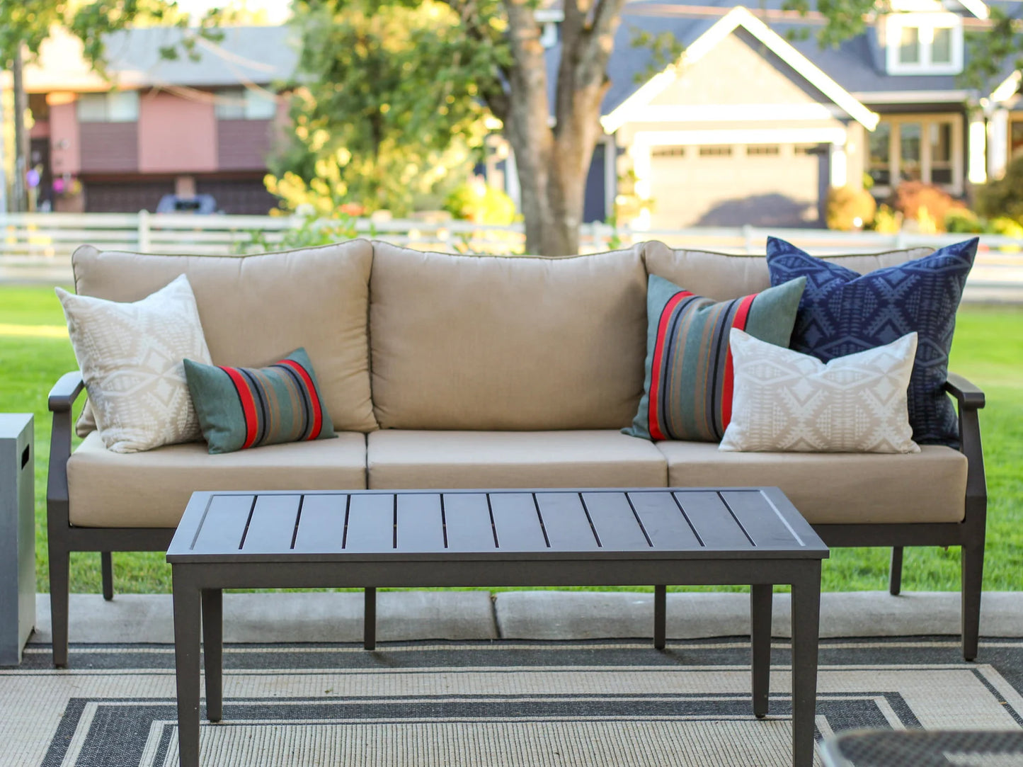 Beige outdoor sofa with colorful outdoor pillows and a matching coffee table on a patio.