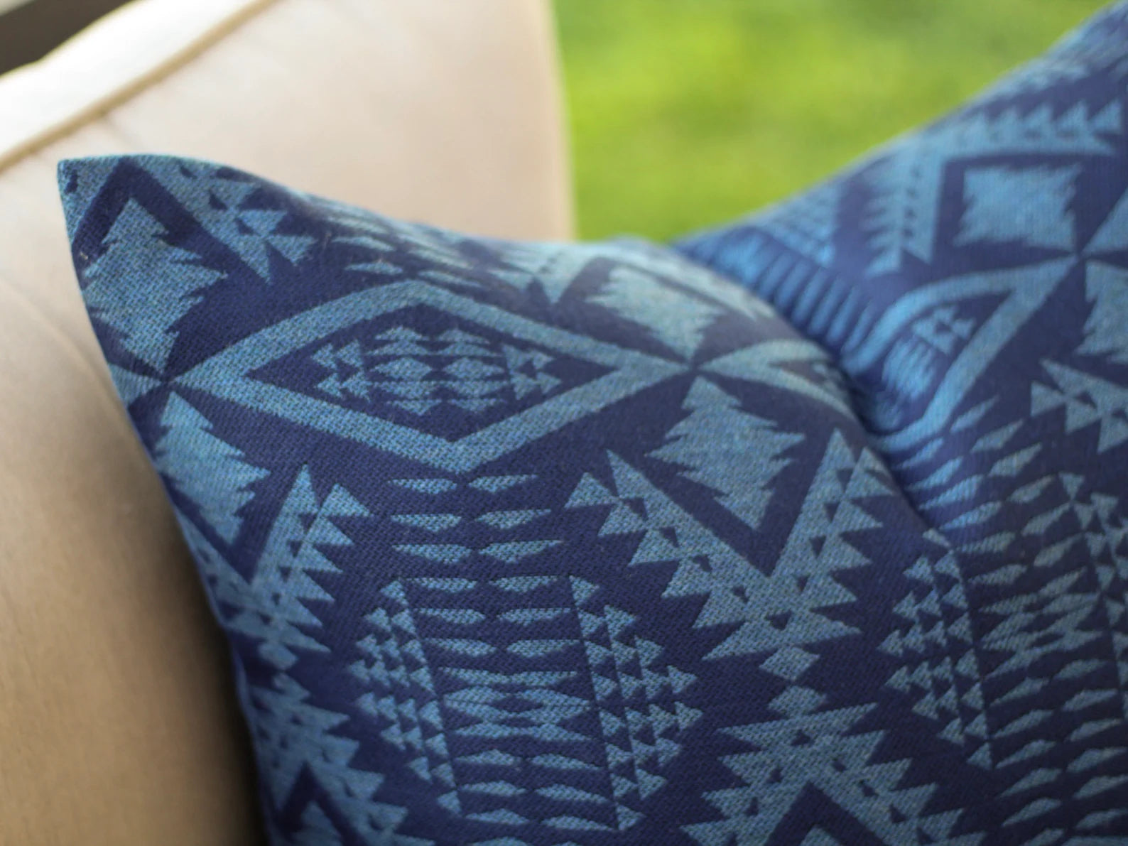 Close up of outdoor pillow in the two-tone blue River Tonal Midnight pattern on a beige surface with a blurred grass background
