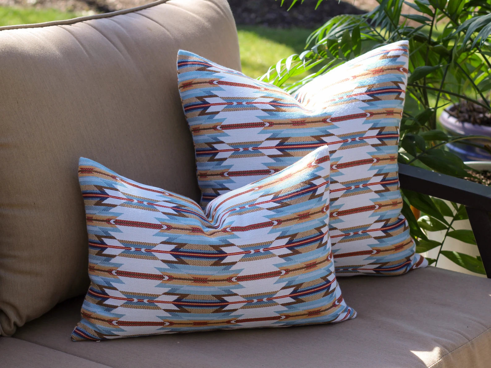Decorative outdoor pillows with the geometric Wyeth Trail Sunset pattern on a beige outdoor sofa.