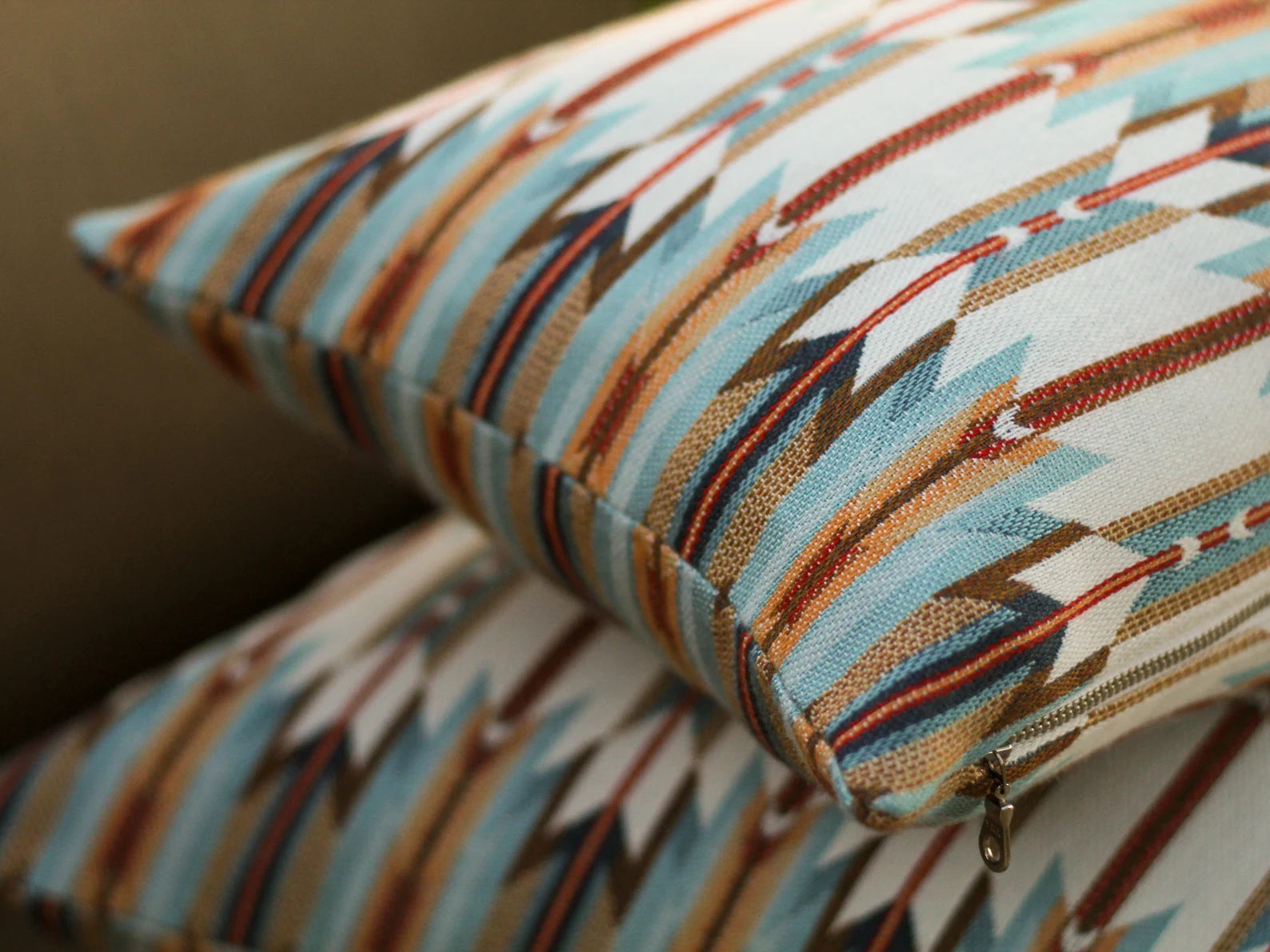 Close up of two outdoor pillow covers in Wyeth Trail Sunset pattern stacked on a neutral background