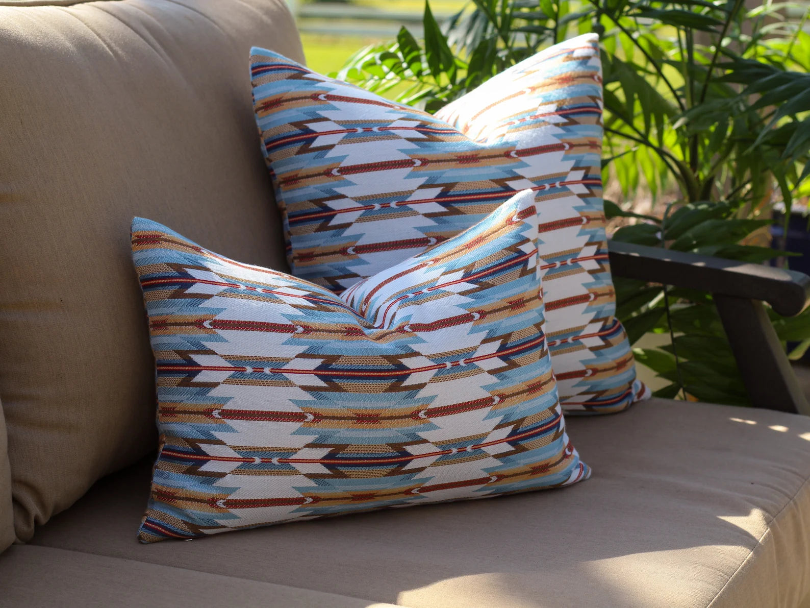 Two patterned pillows in the geometric Wyeth Trail Sunset pattern on a beige outdoor sofa with plants in the background
