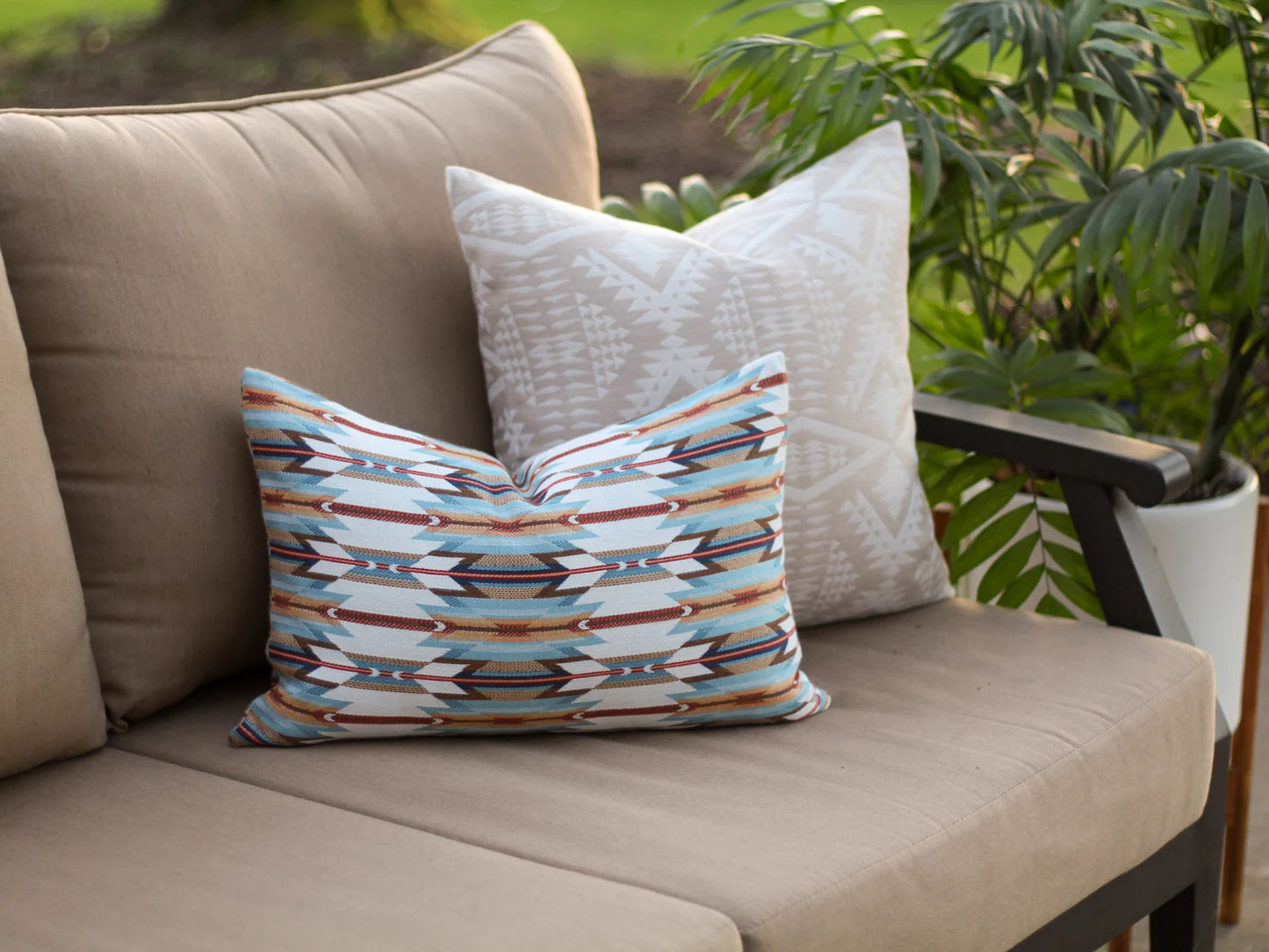 Decorative pillows in the geometric Wyeth Trail Sunset pattern on a beige outdoor sofa with plants in the background