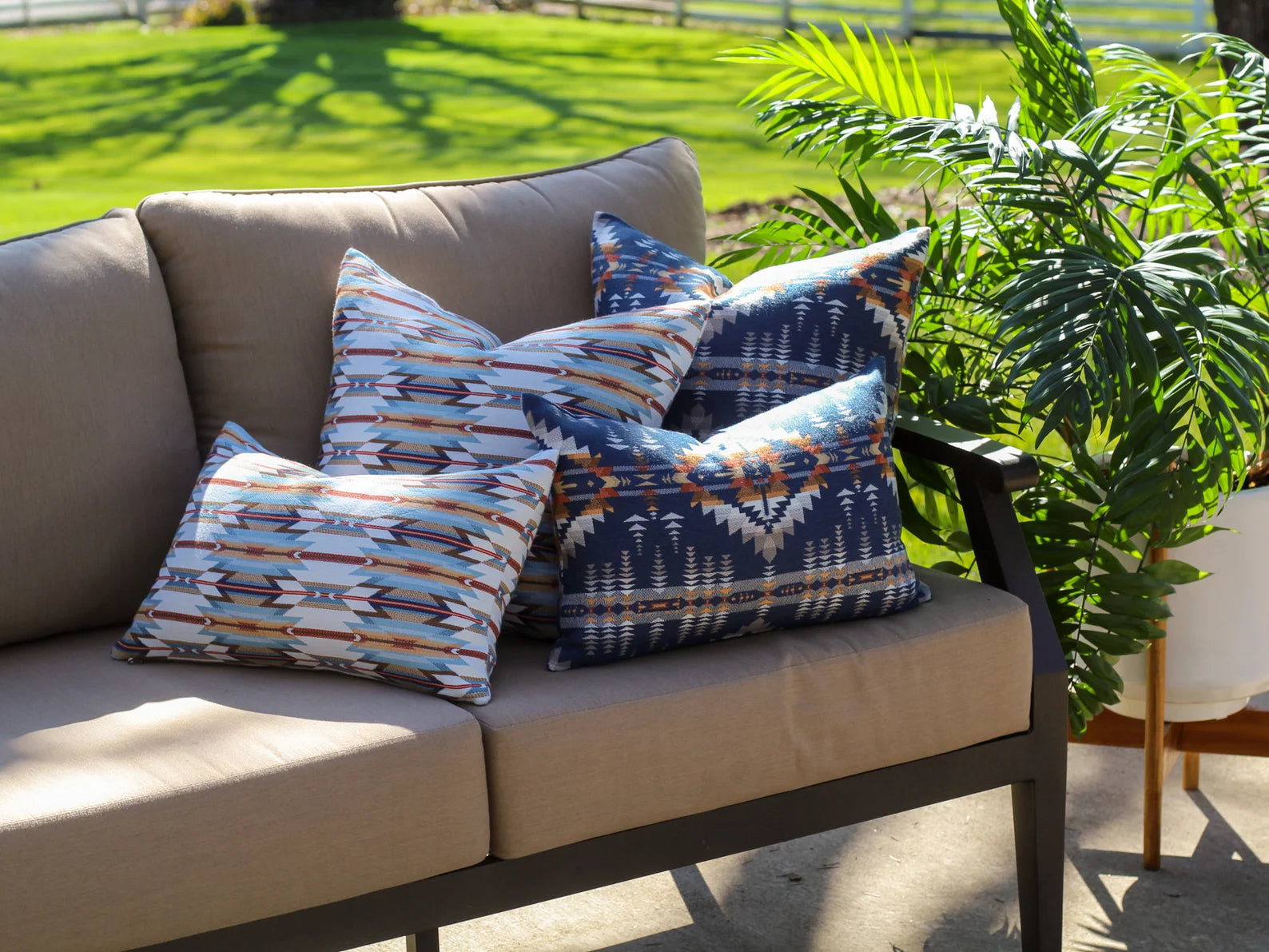 Beige outdoor sofa with patterned outdoor pillow covers surrounded by greenery.