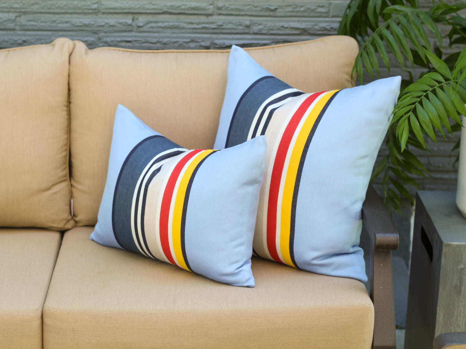Outdoor pillow covers in the Yosemite National Park pattern with blue, red, white, and yellow stripes on a beige sofa.