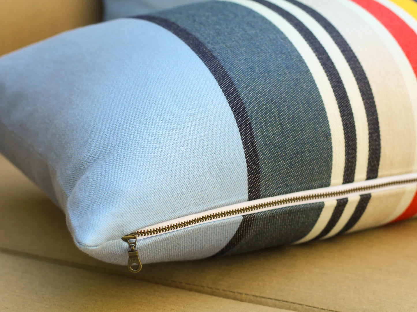 Close up of zipper on pillow cover in the Yosemite National Park pattern with blue, red, white, and yellow stripes on a beige sofa.