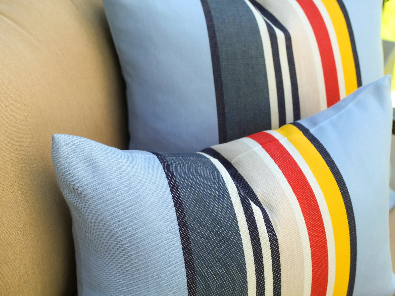 Close up of pillow covers in the Yosemite National Park pattern with blue, red, white, and yellow stripes on a beige sofa.