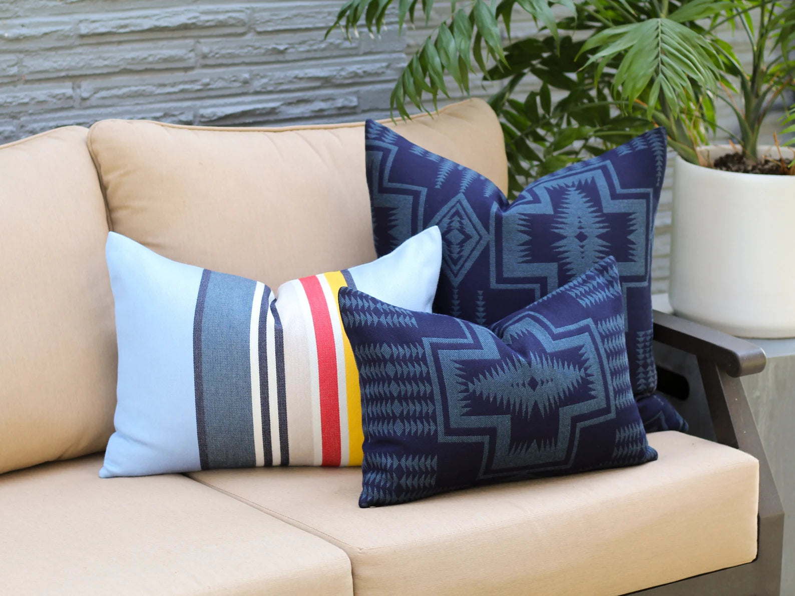Decorative outdoor pillows in the Harding Indigo and Yosemite National Park patterns on a beige outdoor sofa with plants in the background