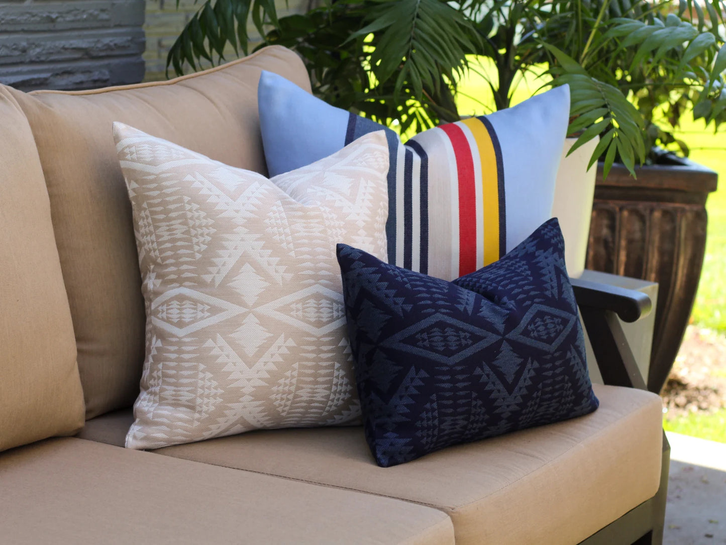 Decorative outdoor pillows on a beige outdoor sofa with plants in the background