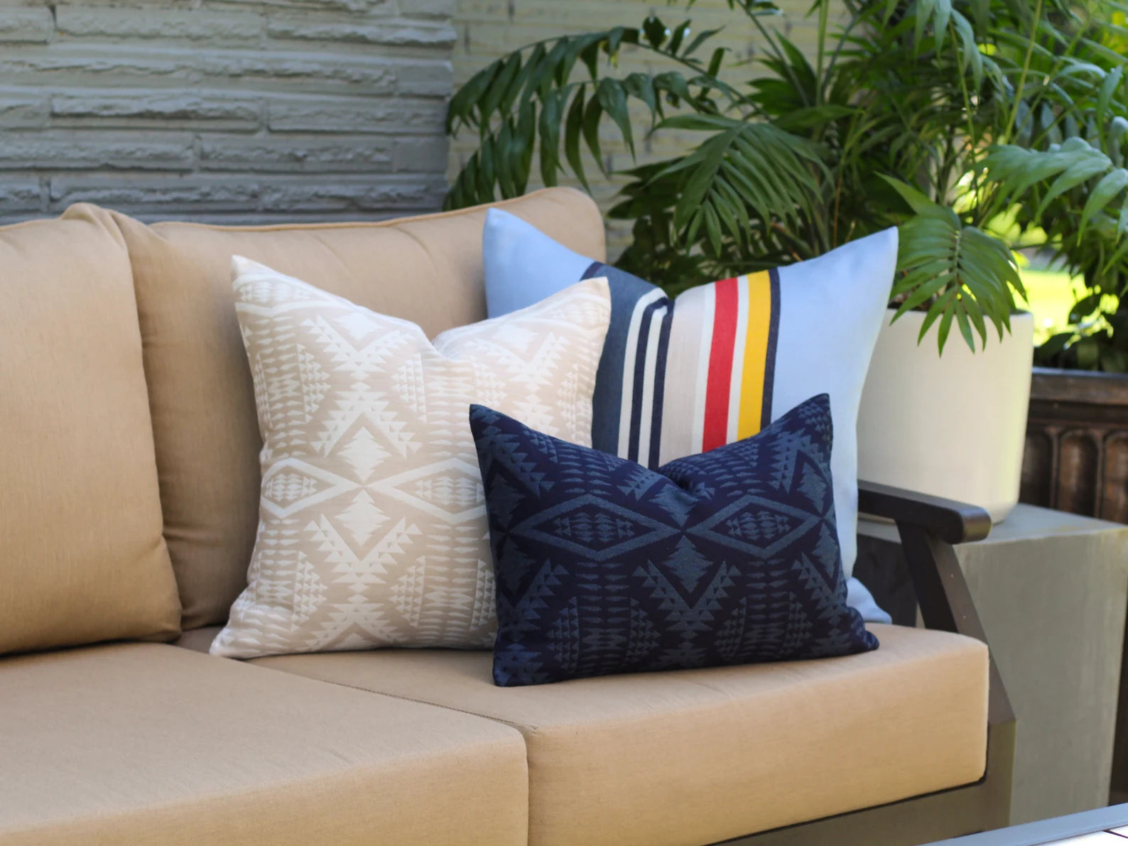 Beige outdoor sofa with outdoor pillows against a stone wall and plants